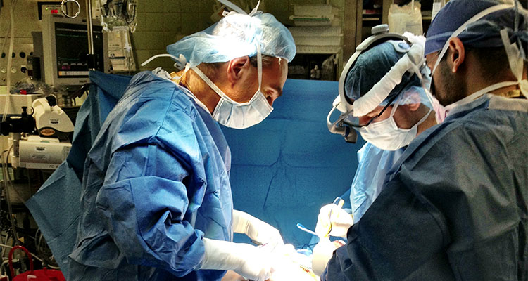 A group of residents are gathered under a bright light and perform surgery