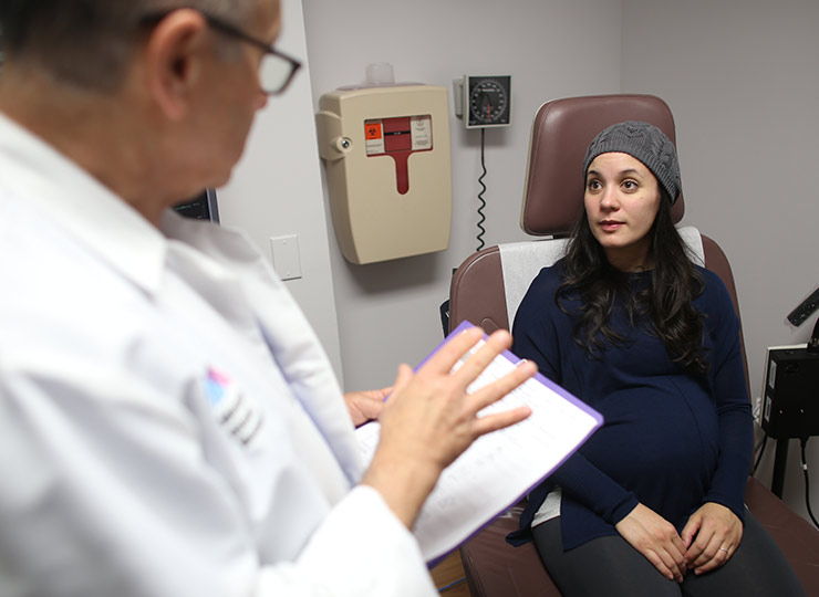 Pregnant patient sitting on exam chair talking to male doctor who is holding a chart